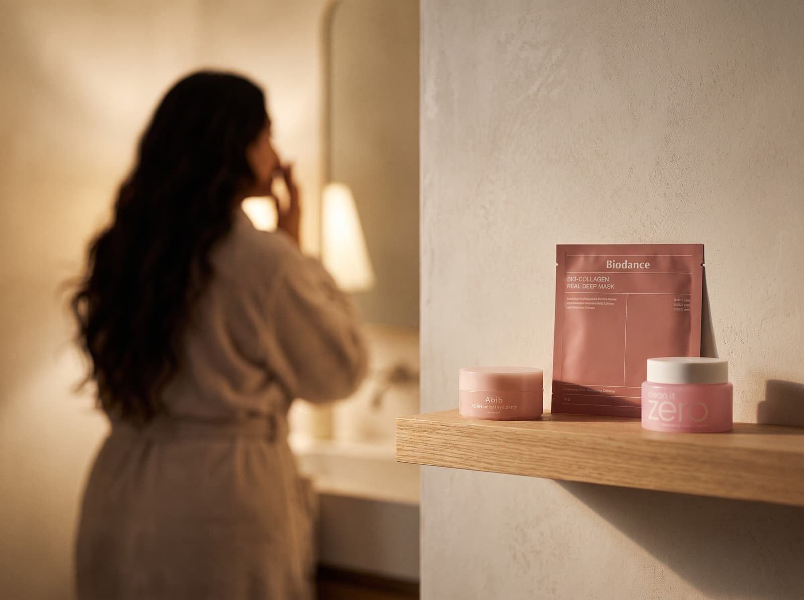 Los productos de Habit Skin en una balda del baño, con Marisol desenfocada al fondo haciéndose la rutina de noche